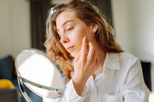 A woman examining her skin closely in the bathroom mirror