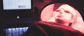 A patient reclined under a red LED phototherapy panel in the Regents Park Aesthetics treatment room